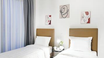 A hotel room with two single beds, a nightstand with a lamp, and artwork on the wall.