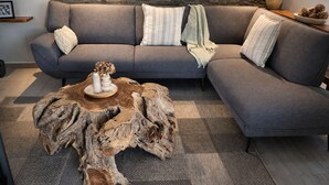A gray sectional sofa with multiple pillows and a woven coffee table with a vase.