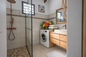 A bathroom with a shower, washing machine, wooden vanity, and a mirror.