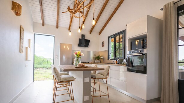 A modern kitchen with a central island, bar stools, a chandelier, and a view of the outdoors.