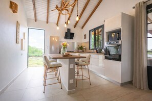 A modern kitchen with a central island, bar stools, a chandelier, and a view of the outdoors.