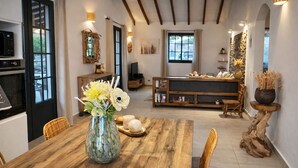 A dining area with a wooden table, chairs, a vase with flowers, and a rustic wall decoration.
