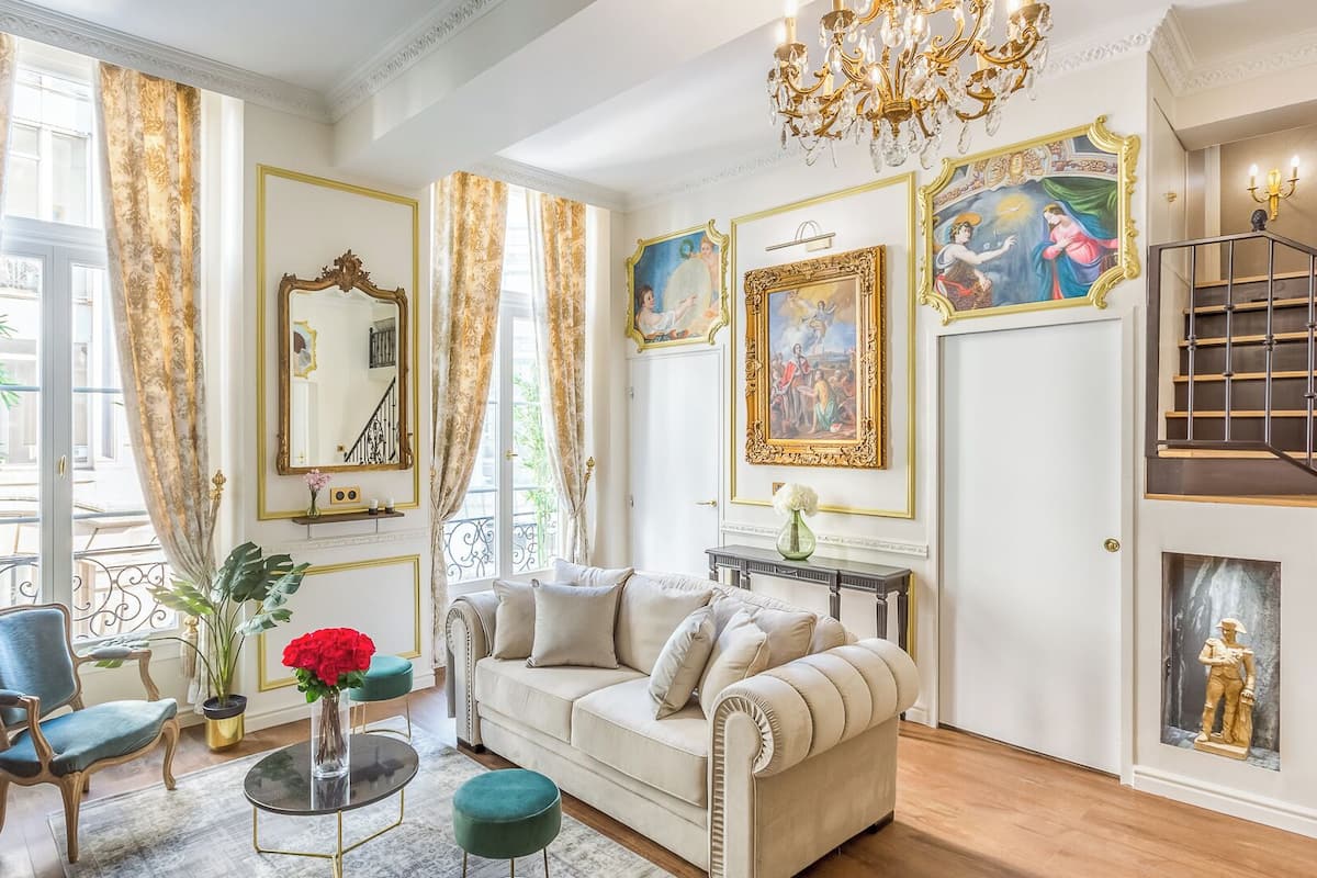 A spacious living room with a high ceiling, a chandelier, and a staircase with a railing.