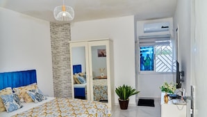 A bedroom with a bed, a wardrobe, a potted plant, a desk with a computer, and a window with a view. - RESIDENCES CHELIEL, Morofé youth hostels (Yamoussoukro)