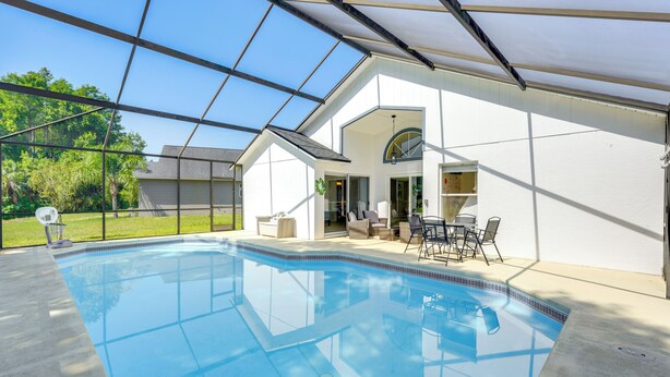 Zwembad met glazen dak, omgeven door een wit gebouw met een patio en tuinmeubilair.