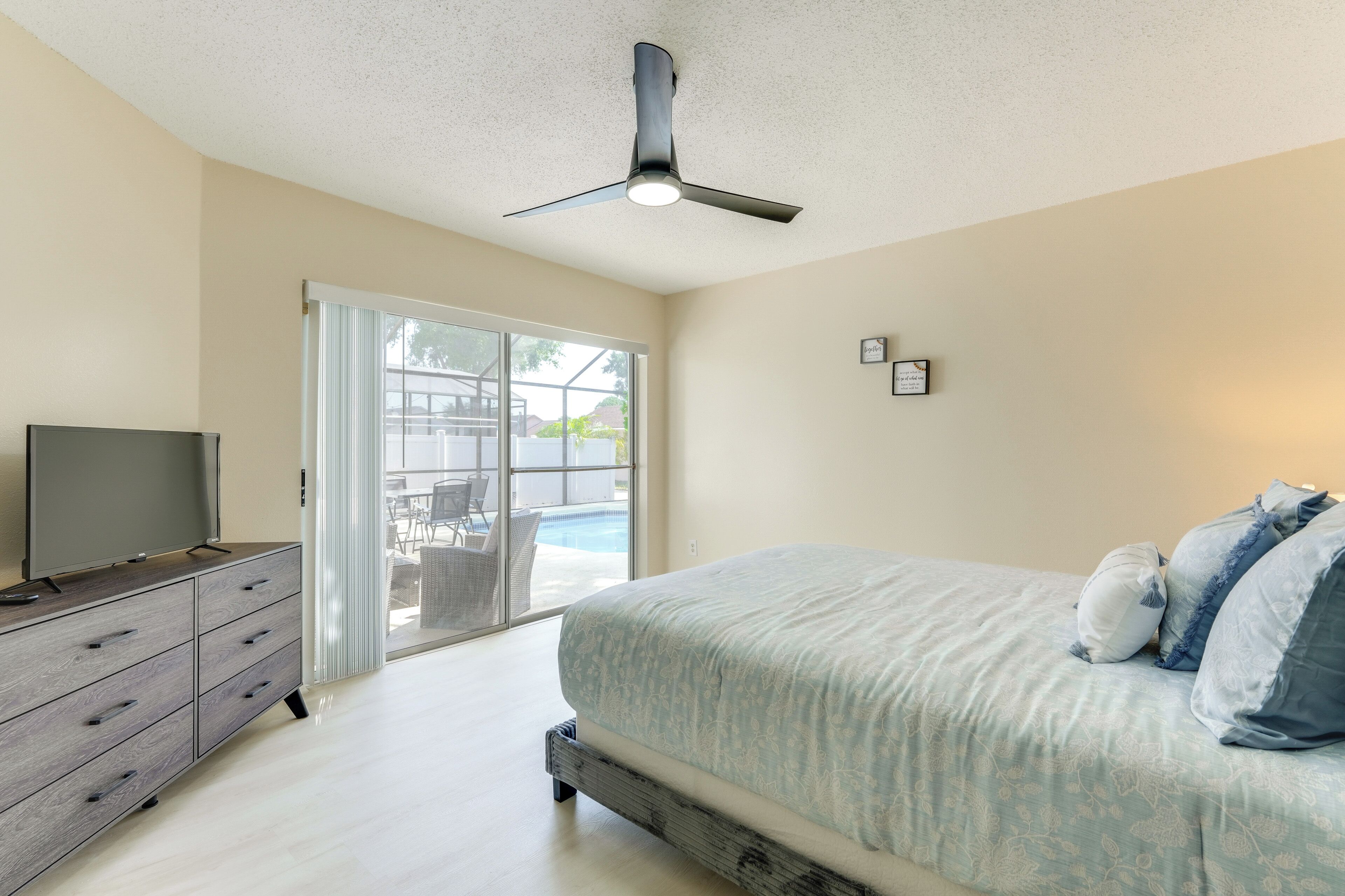 A bedroom with a bed, a TV on a dresser, a ceiling fan, and a sliding glass door leading to a patio.