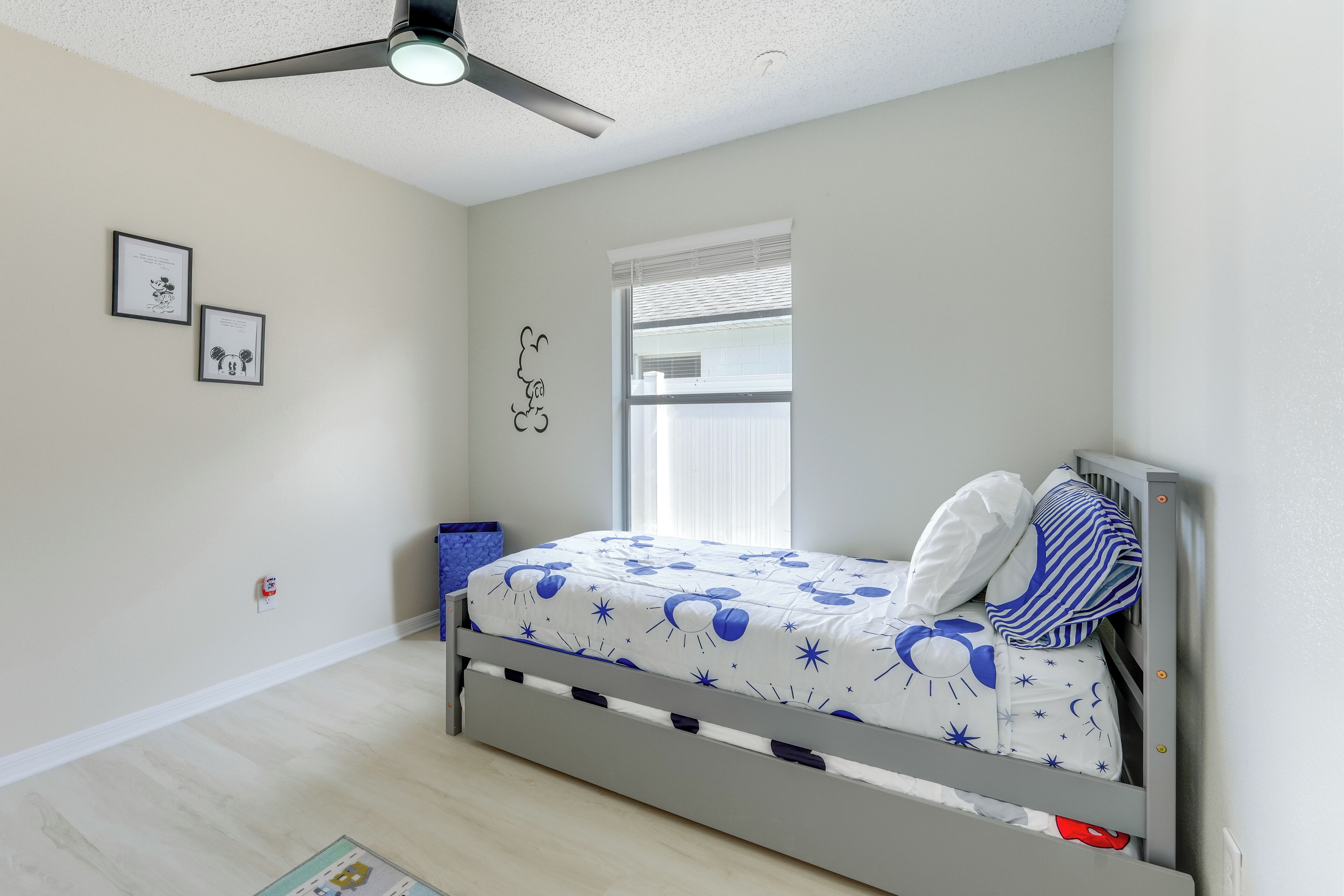 Un dormitorio con cama, ventilador de techo, ventana y adornos en la pared.