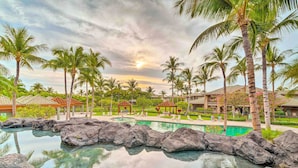 Piscina de resort con bordes de piedra, rodeada de palmeras y un pabellón.
