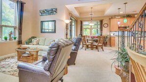 Amplia sala de estar con sofá, sillas, una mesa de comedor y una zona de cocina con armarios de madera y una escalera.
