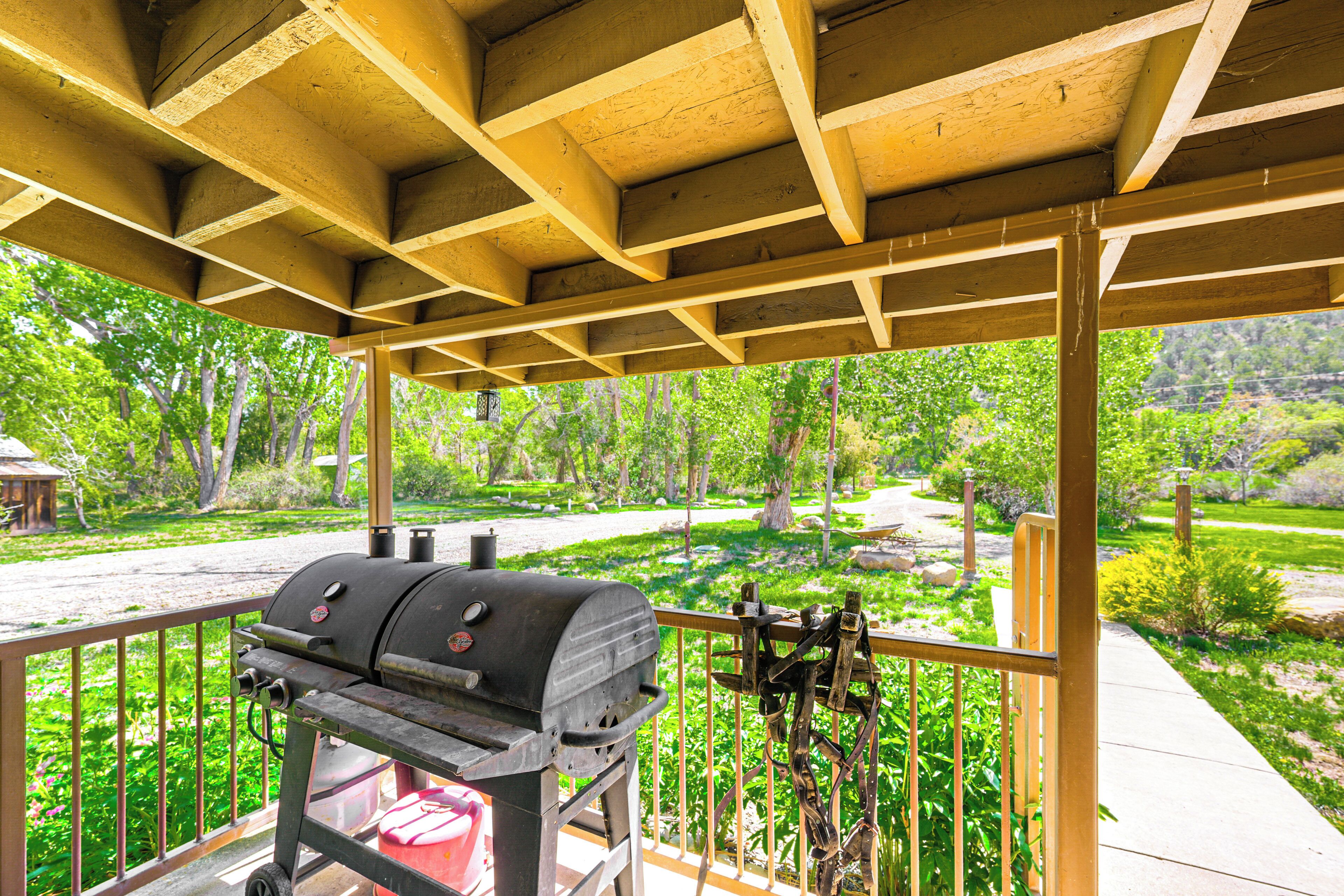 A covered outdoor area with a barbecue grill, wooden beams, and a view of a landscaped garden.