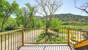 A wooden deck with a metal railing overlooking a park with trees and a hilly landscape.