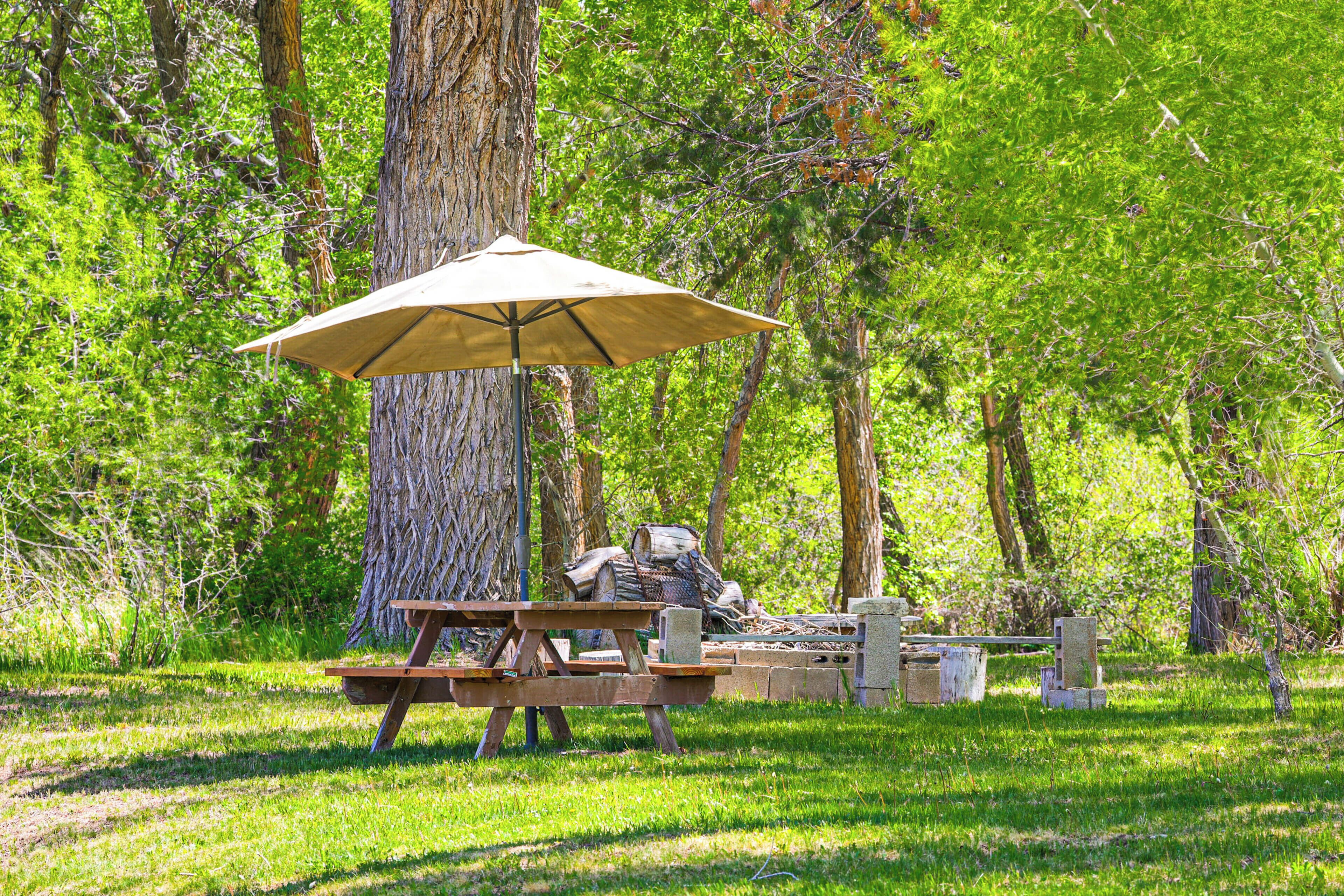 Een picknickplaats met een tafel, bank en parasol in een bebost gebied.