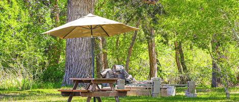 Een picknickplaats met een tafel, bank en parasol in een bebost gebied.