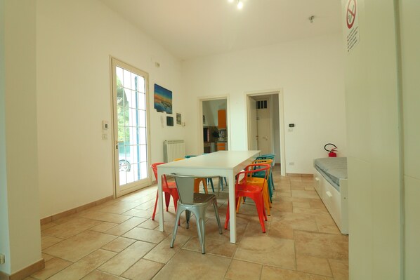 A spacious room with a large dining table surrounded by colorful chairs, a white bed, and a radiator. - Villa in Salento - 10 minute from the sea (Nardò)