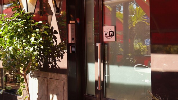 Une entrée d’immeuble avec un auvent rouge, un panneau indiquant la présence d’un réseau Wi-Fi et un pot de fleurs.