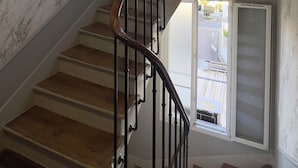 Un escalier en colimaçon avec des marches en bois et des rampes en métal, menant à un palier doté d’une fenêtre.