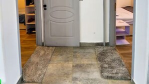A hallway with a grey door, wooden flooring, and two rugs leading to a bedroom with a bed and a nightstand. - 2 BRs Urban Oasis: Airport & Metro (Cairo Governorate)