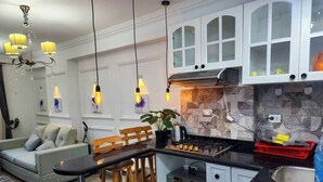 A modern kitchen with white cabinets, a black countertop, and a built-in oven. There is a dining area with a wooden table and chairs, and a chandelier hanging above. - 2 BRs Urban Oasis: Airport & Metro (Cairo Governorate)