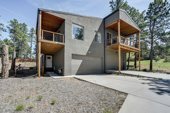 A modern two-story house with a garage, wooden balconies, and a clear view of the surrounding forest.