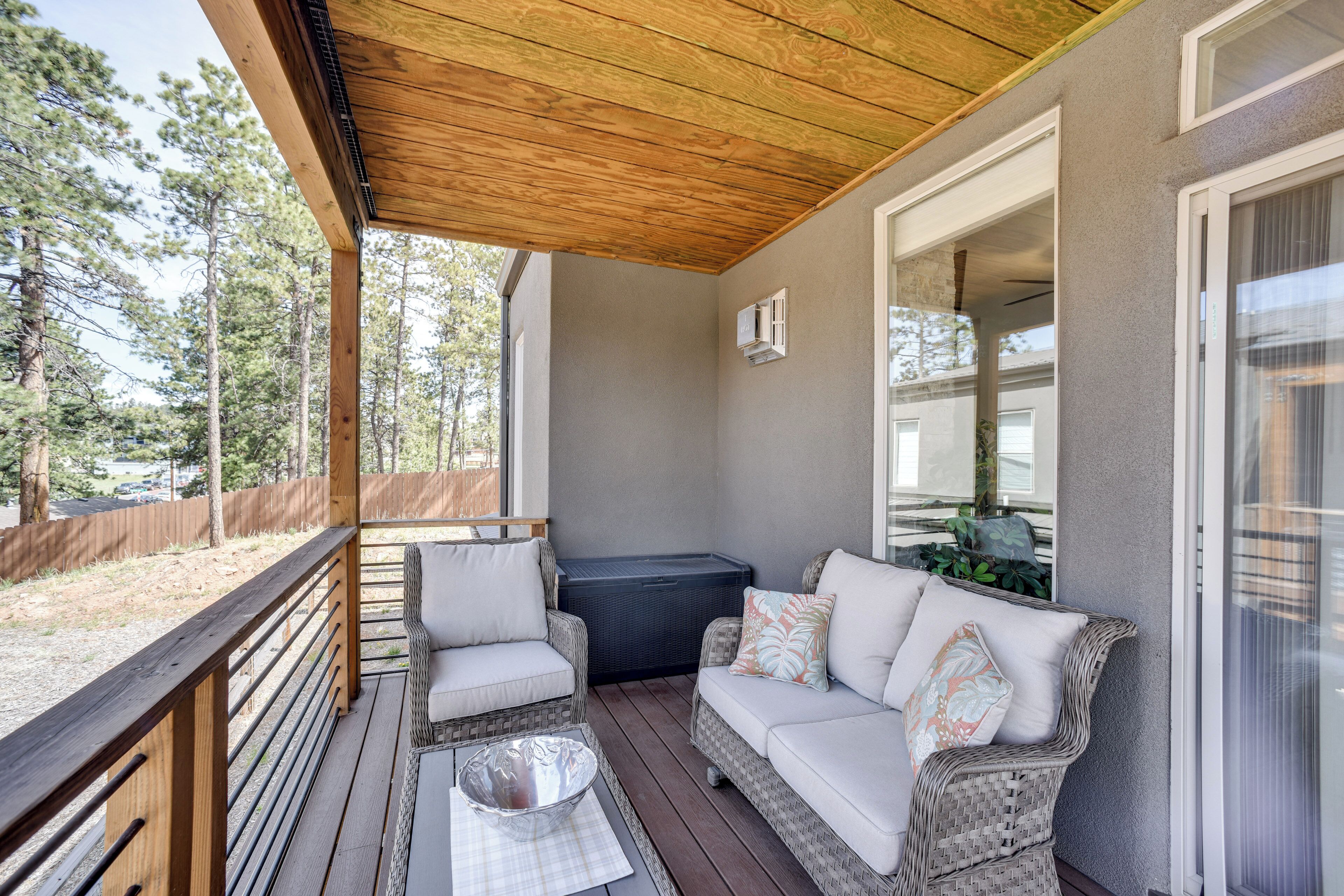 A covered porch with wicker furniture, a hot tub, and a view of a forest.