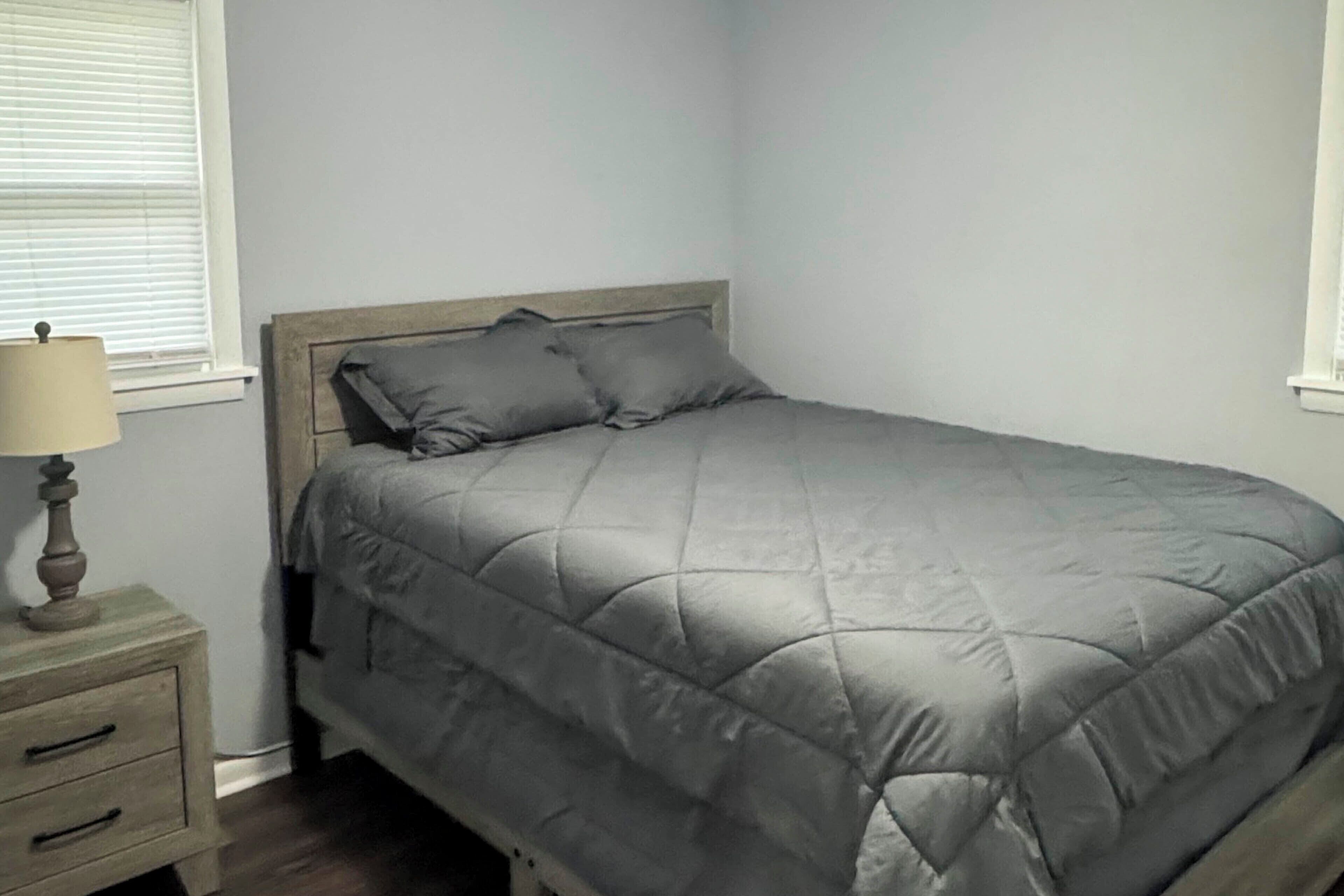 Une chambre à coucher avec un lit, une table de chevet avec une lampe et une fenêtre avec des stores.