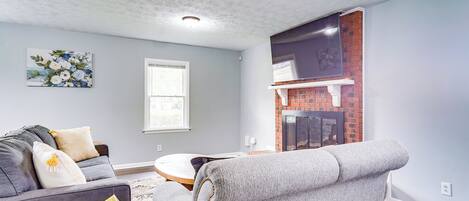 A living room with a gray sofa, a gray armchair, a small round table, and a fireplace.