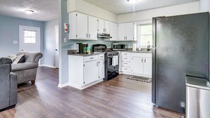 A modern kitchen with white cabinets, a stainless steel refrigerator, and a gray sofa in a living area. - 5 Mi to Dtwn: Family-friendly Fayetteville Home! (Fayetteville)