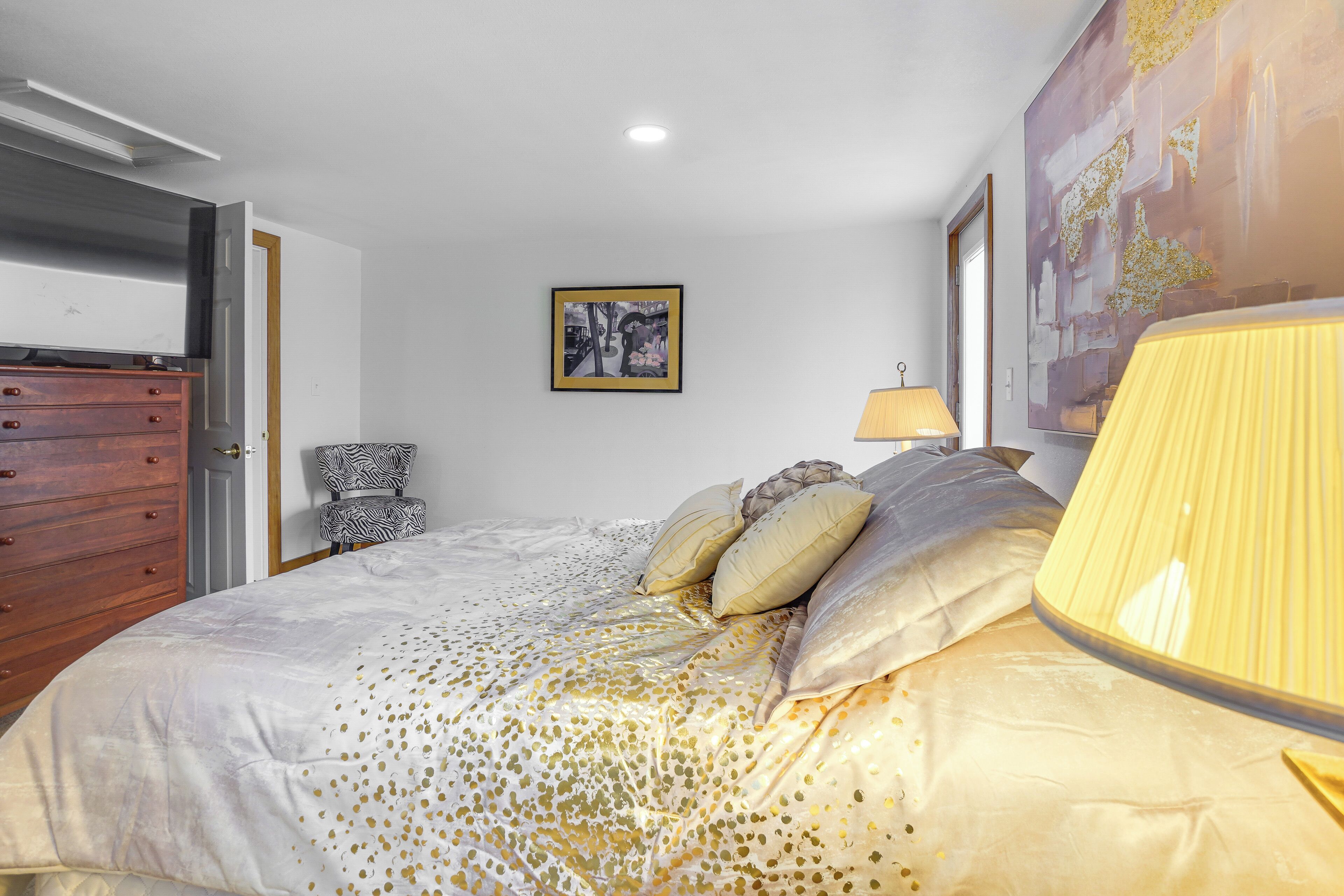 A bedroom with a bed, a wooden dresser, a chair, and a painting on the wall.