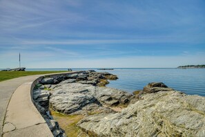 A coastal walkway with a concrete path, rocky shoreline, and a flagpole.
