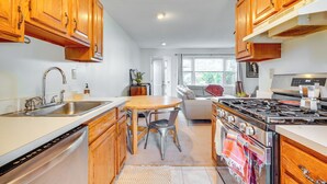 Une cuisine avec des meubles de rangement en bois, un évier en acier inoxydable, une table à manger avec des chaises, une cuisinière et un réfrigérateur.