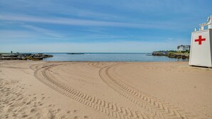Une plage de sable où l’on voit des traces de pneus menant à un bâtiment blanc orné d’une croix rouge.