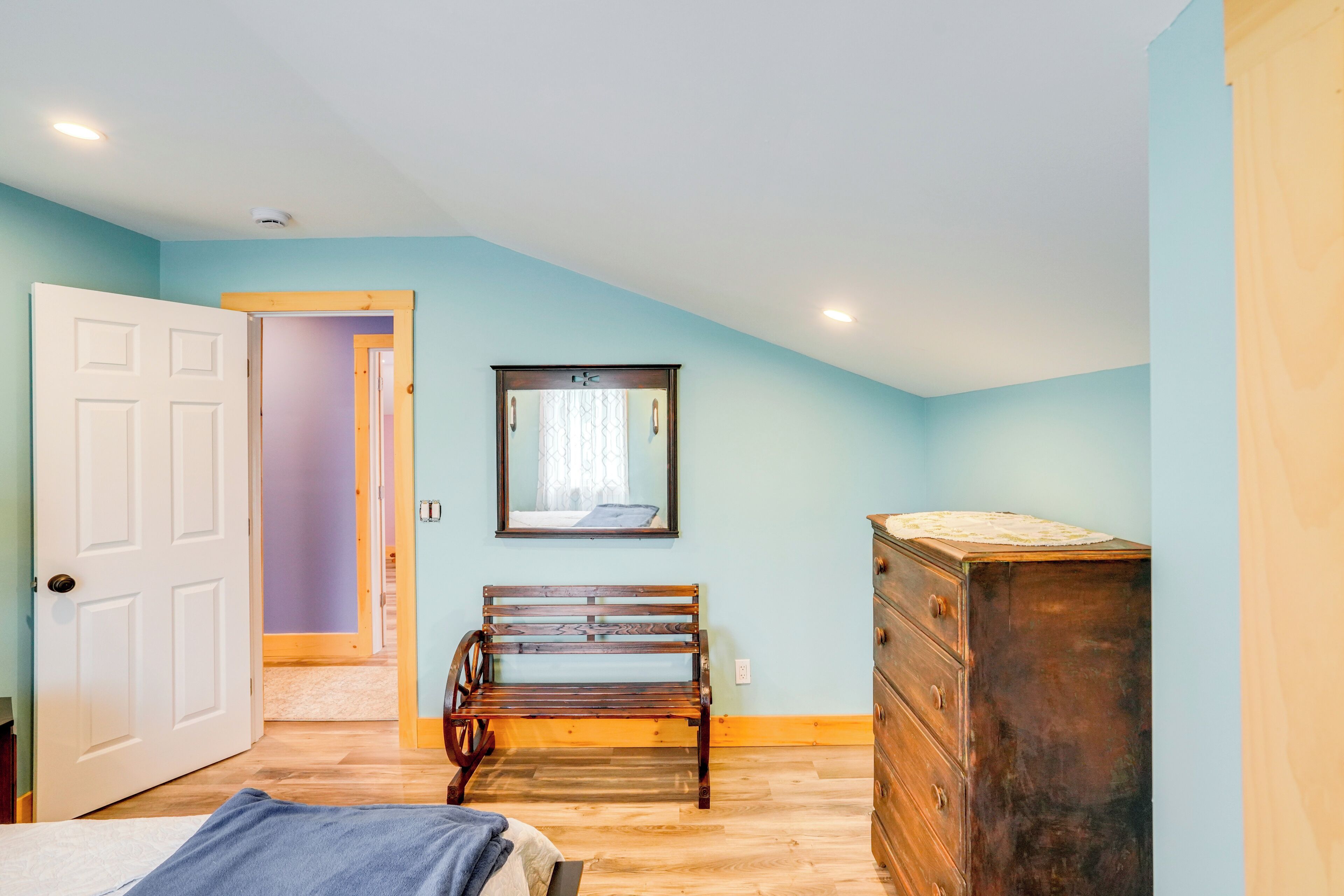 A bedroom with a wooden bench, a dresser, and a door leading to another room.