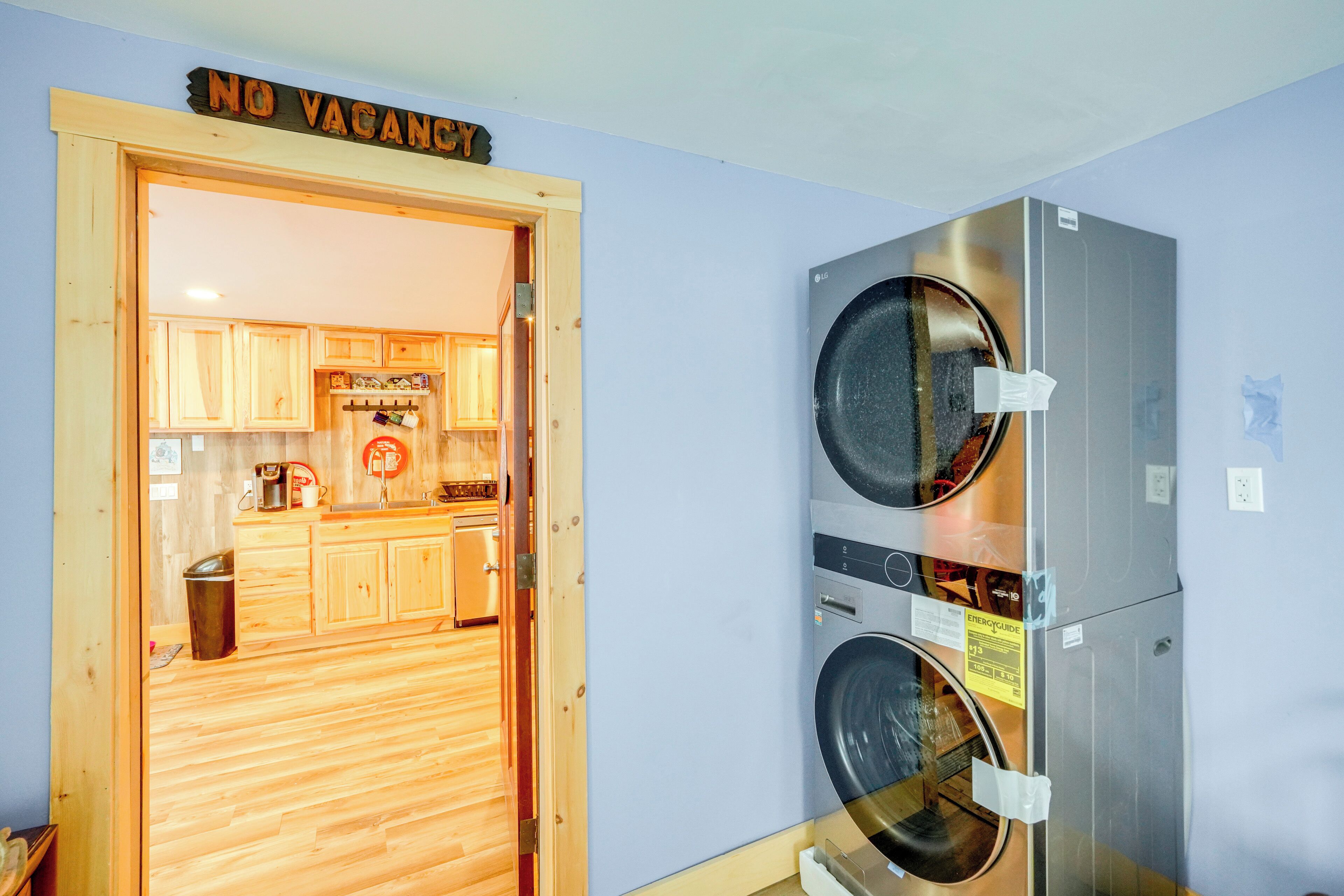 A laundry room with two stacked front-loading washing machines and a wooden door with a 'NO VACANCY' sign.