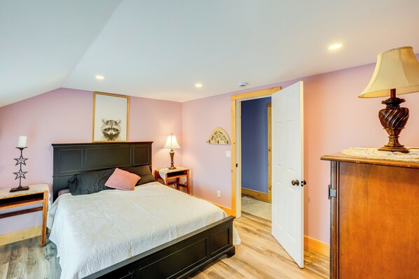 Un dormitorio con cama, mesita de noche, lámpara y una puerta que da a otra habitación.