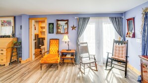 Een kamer met een houten vloer, een gele fauteuil, een schommelstoel, een houten dressoir en een spiegel aan de muur.