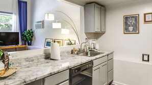 A modern kitchen with a marble countertop, built-in dishwasher, and a window with blue curtains. - 7 Mi to Dtwn: Charming Couple's Cove in Cincinnati (Cincinnati)