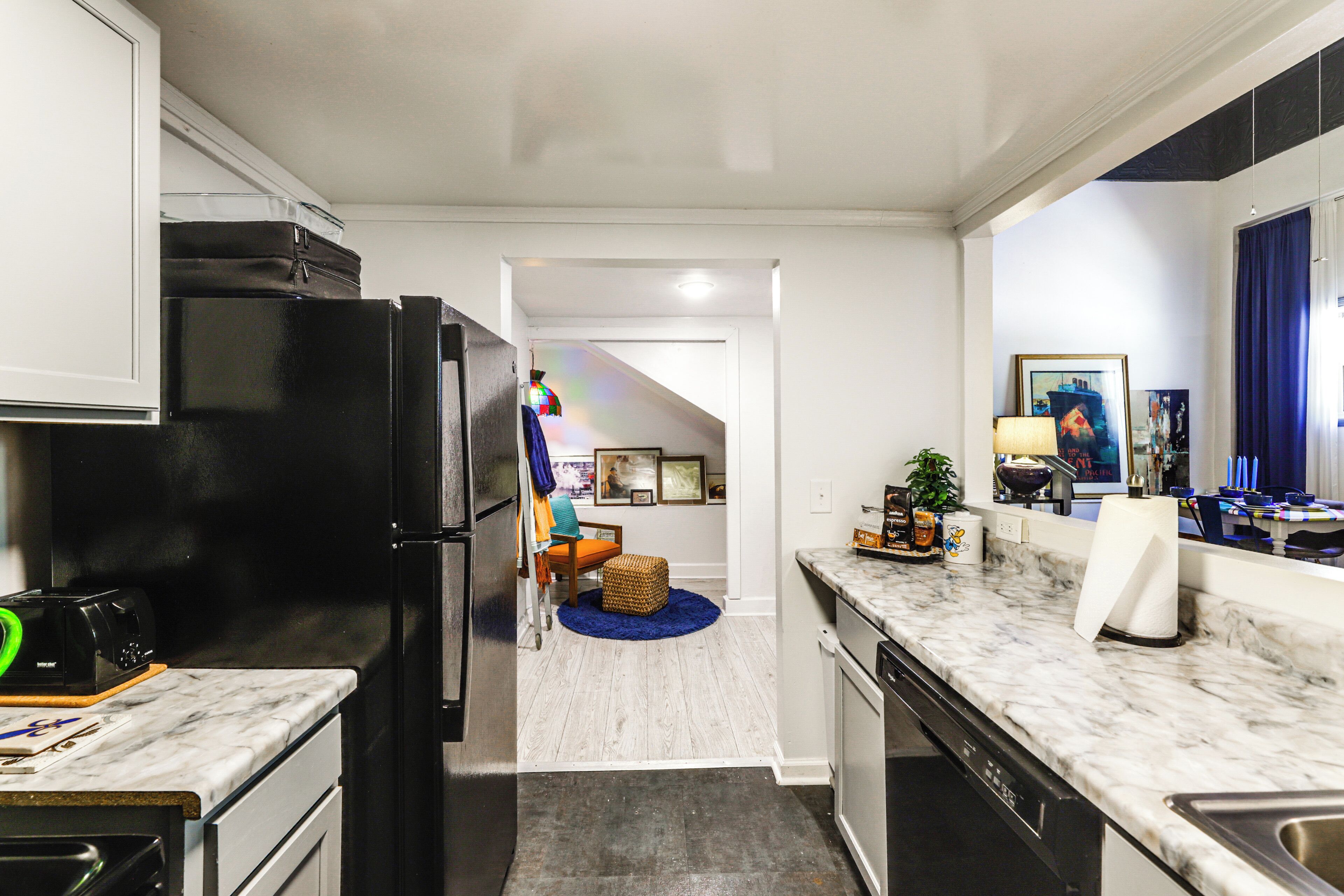 A kitchen with a black refrigerator, a microwave, and a sink. There is a dining area with a table and chairs, and a blue rug on the floor.