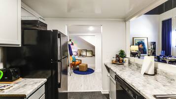 A kitchen with a black refrigerator, a microwave, and a sink. There is a dining area with a table and chairs, and a blue rug on the floor.