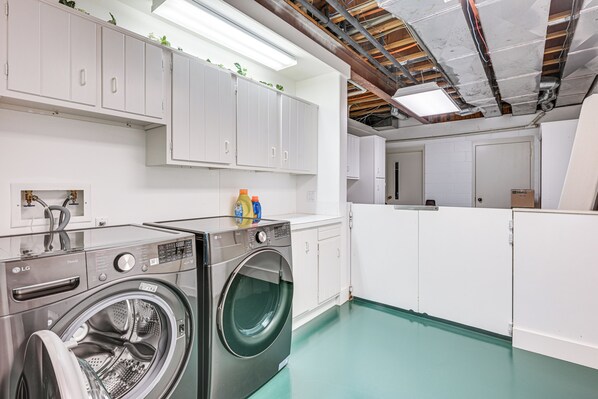 A laundry room with a front-loading washer and dryer, white cabinets, and a green floor.