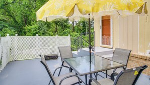Un patio al aire libre con una mesa de vidrio y cuatro sillas, un paraguas amarillo y una cerca blanca.