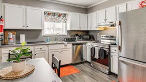 Una cocina moderna con gabinetes blancos, electrodomésticos de acero inoxidable y una isla central con una planta en maceta.