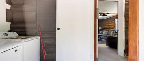 Un área de lavandería con una lavadora y una escoba roja apoyada en la pared.