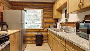 A log cabin kitchen with wooden cabinets, a stainless steel refrigerator, a sink, and a window with blinds. - Hike, Bike & Explore: Woodsy Retreat in Mt Laguna! (Mount Laguna)