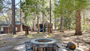 A forested campsite with a circular fire pit, wooden play structures, and a small cabin. - Hike, Bike & Explore: Woodsy Retreat in Mt Laguna! (Mount Laguna)