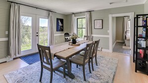 A dining area with a wooden table, four chairs, a rug, and a bookshelf. - Pond Views: Spacious Family Home in Presque Isle! (Presque Isle)