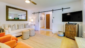 Un salon avec un canapé, un pouf et un téléviseur posé sur un meuble en bois.