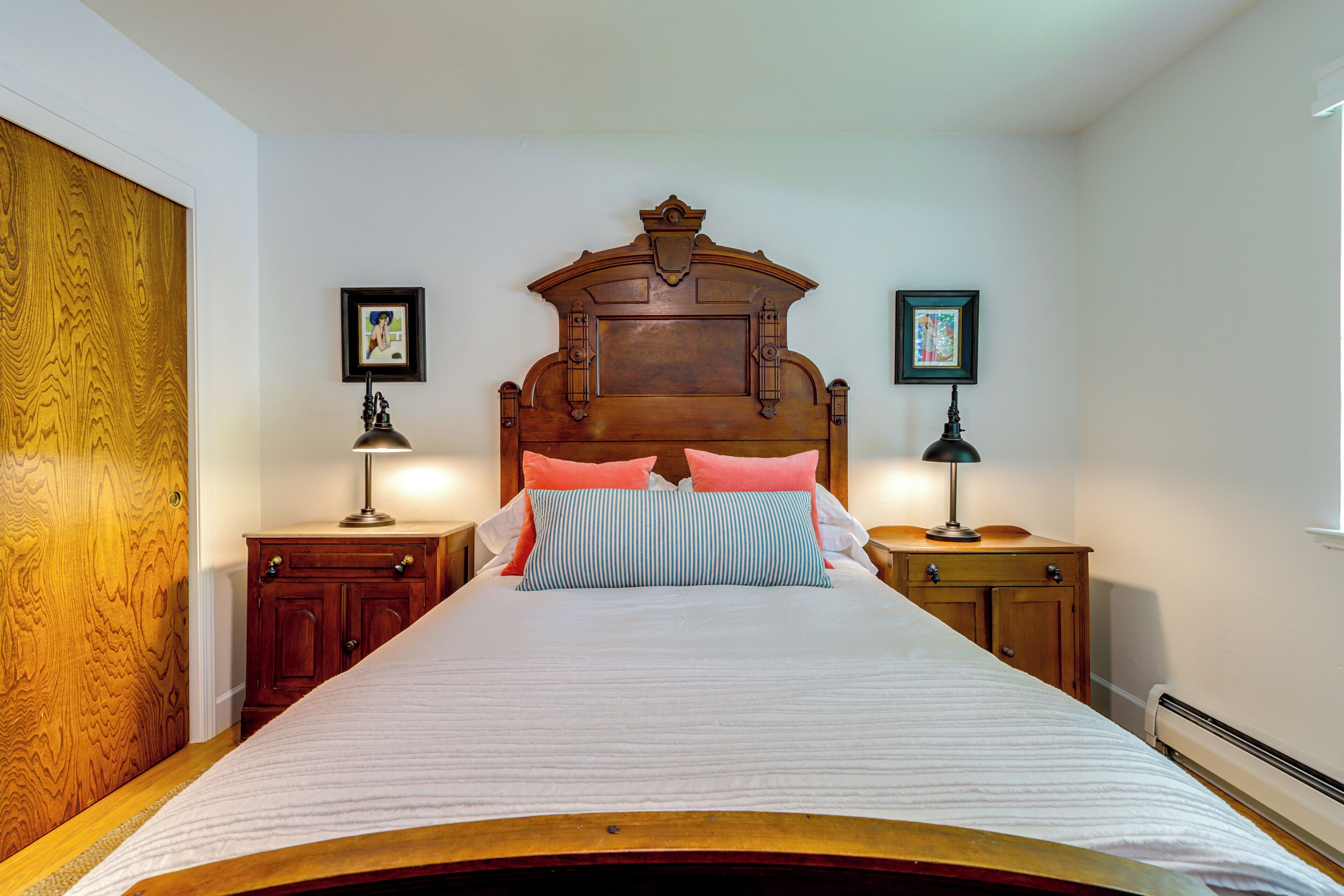 A neatly made bed with a wooden headboard, two bedside tables with lamps, and framed pictures on the walls.