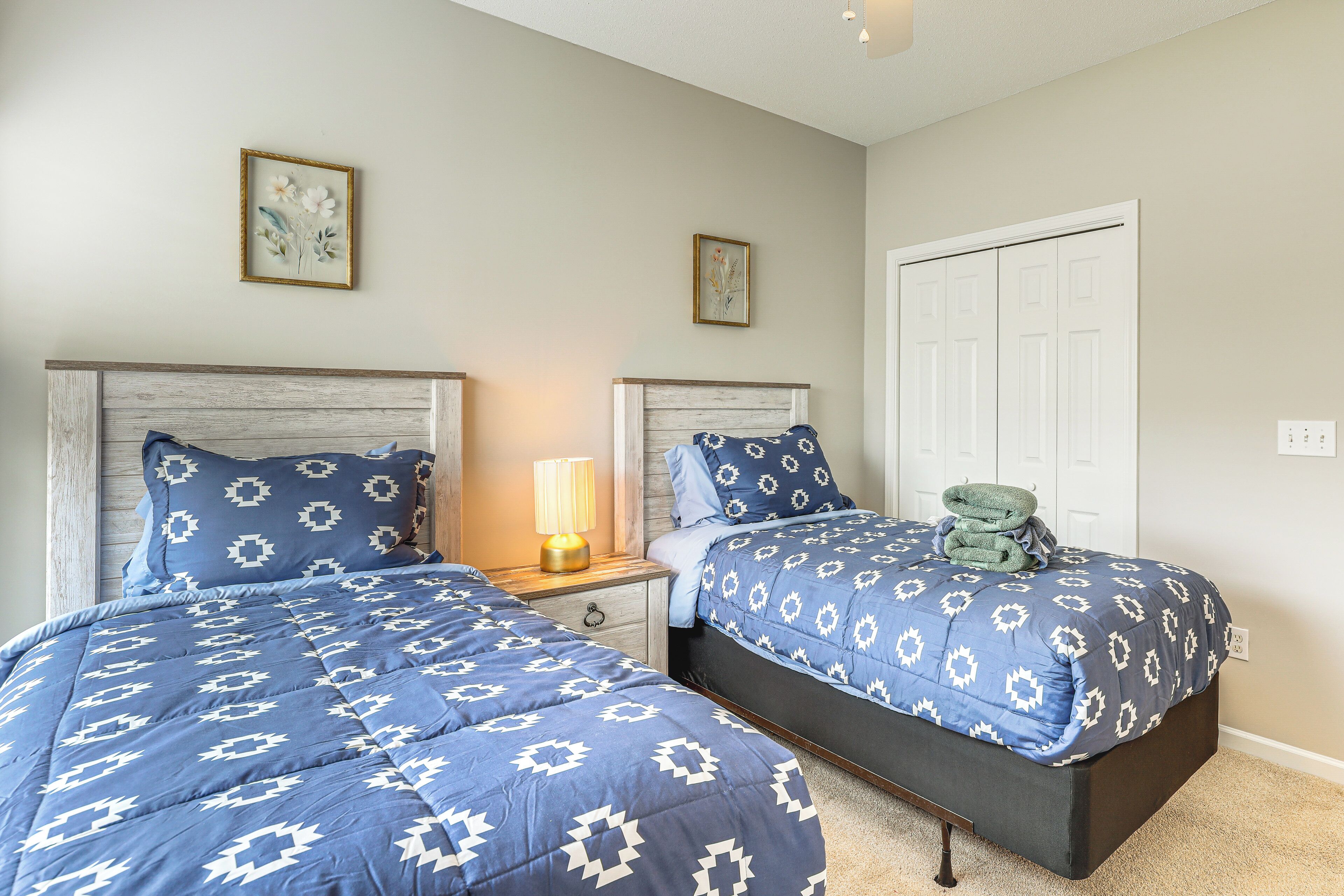 Un dormitorio con dos camas, cada una con una colcha azul estampada y almohadas a juego. Entre las camas hay una mesita de noche con una lámpara.