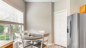 A kitchen with a round table, white chairs, a stainless steel refrigerator, and a window with blinds. - < 1 Mi to Legends Golf Resort: Condo w/ Pool! (Myrtle Beach)