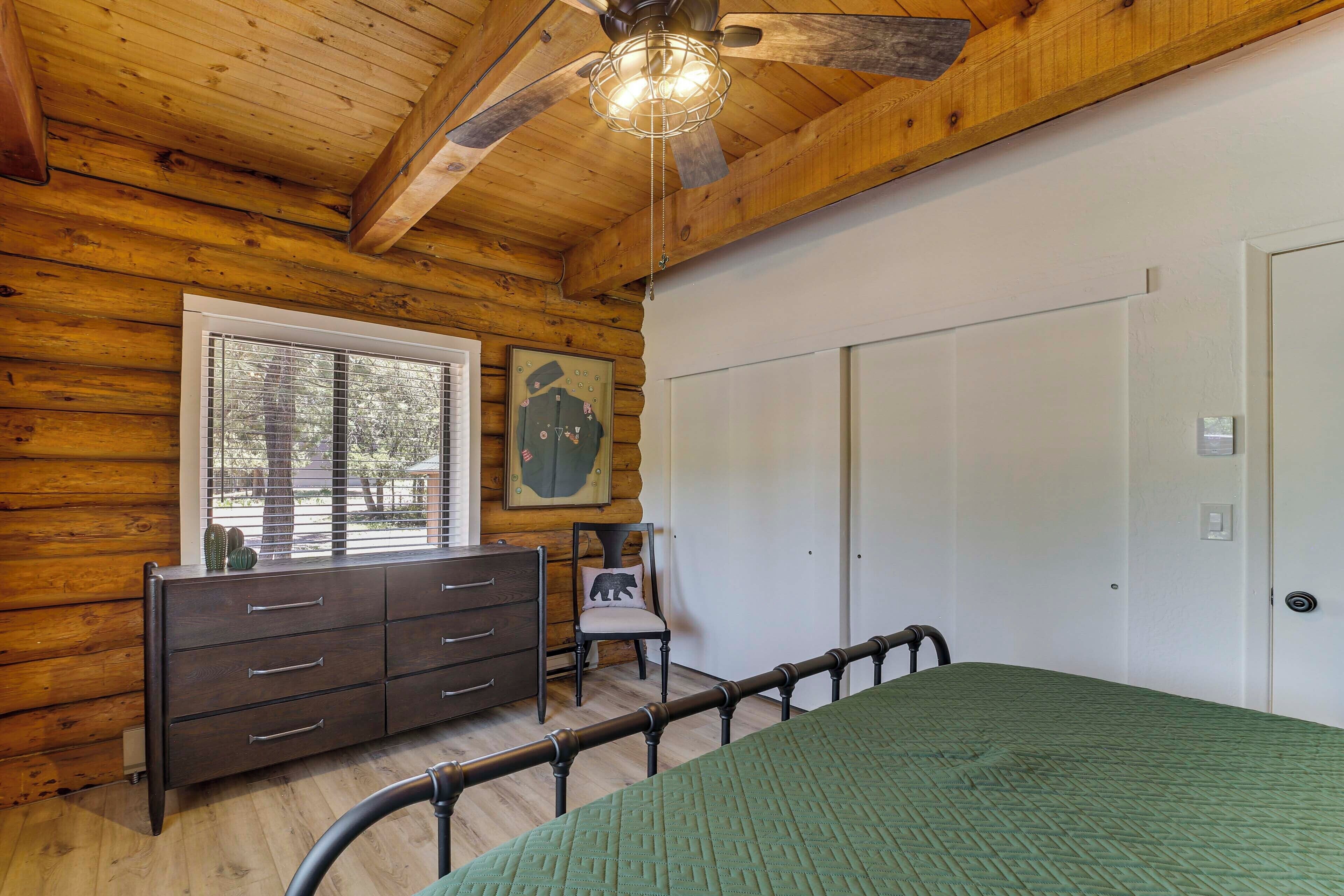 Ein Schlafzimmer einer Holzhütte mit Bett, Schminktisch, Stuhl und großem Fenster.